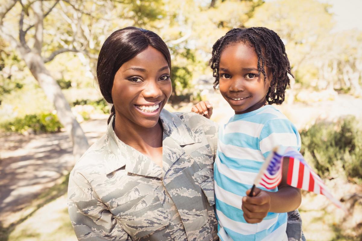 A service member stands for a picture with her young child