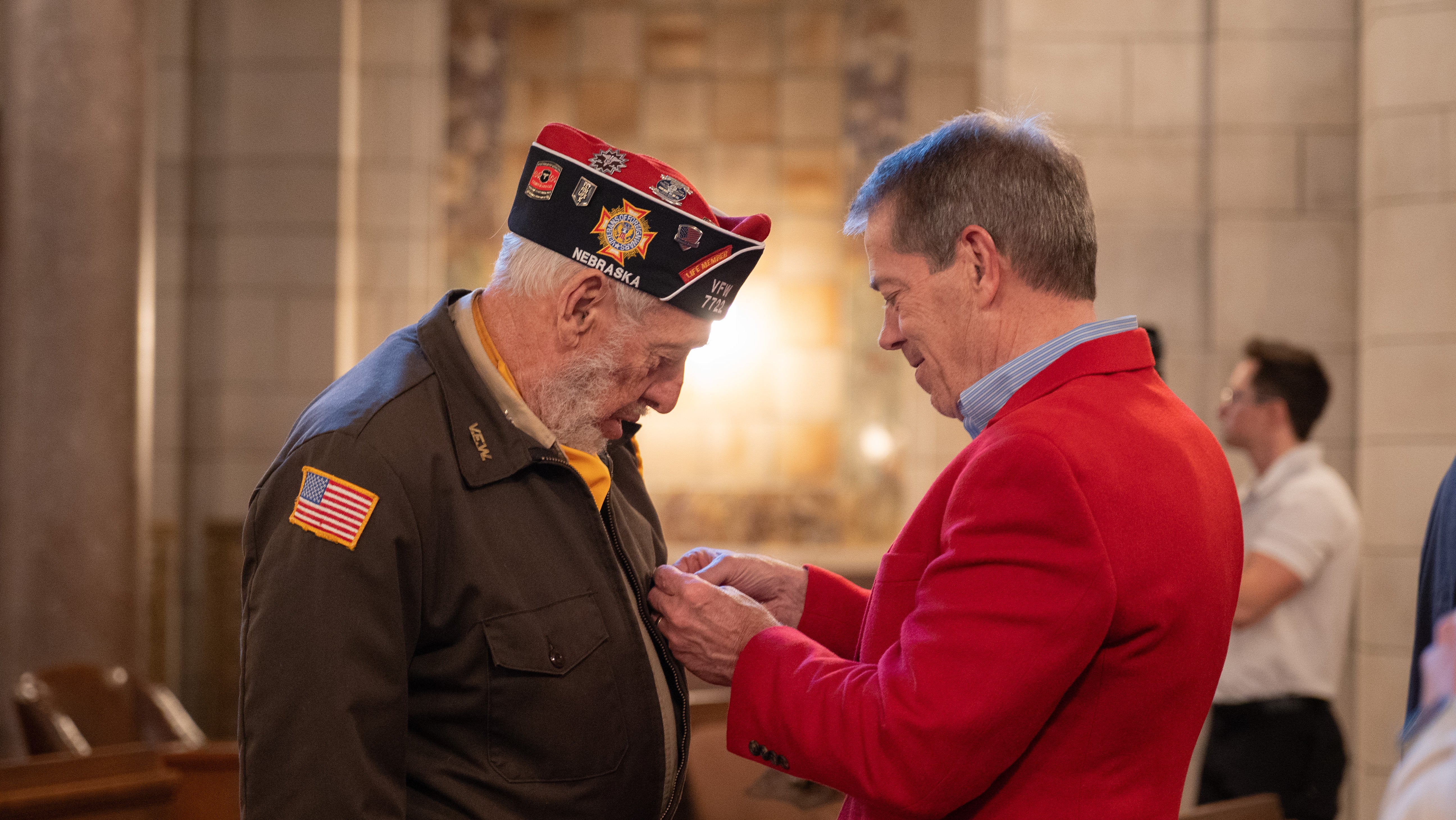Gov. Pillen pins a Vietnam War lapel pin on a veterans’ jacket at the State of Nebraska’s Vietnam War Veterans Day ceremony