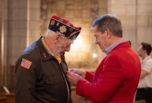 Gov Pillen pins Vietnam War lapel pin on veteran's lapel during Vietnam War Veterans Day ceremony