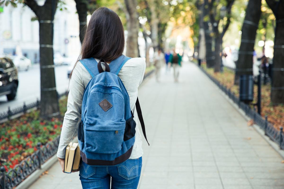 female student walking outside away from camera with blue backpack
