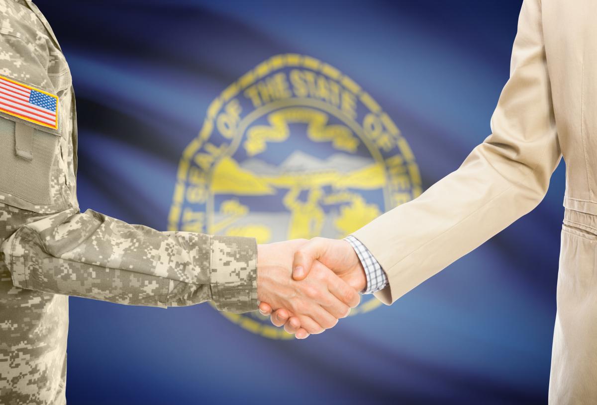 military service member shaking hands with a business person in front of the flag of Nebraska